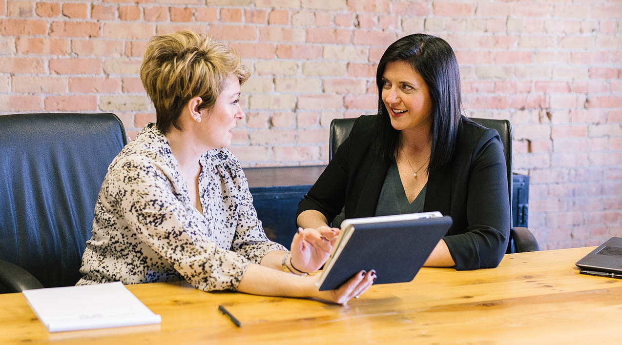 Two women talking at desk with tablet